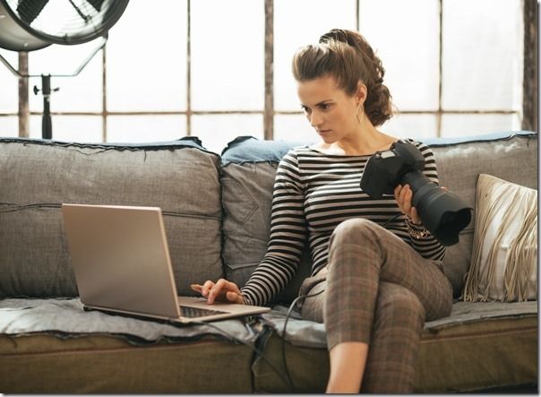 Young woman with modern dslr photo camera using laptop in loft apartment