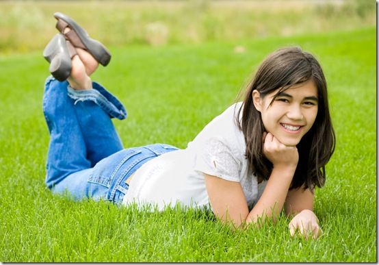 Young teen girl lying on green grass, relaxing