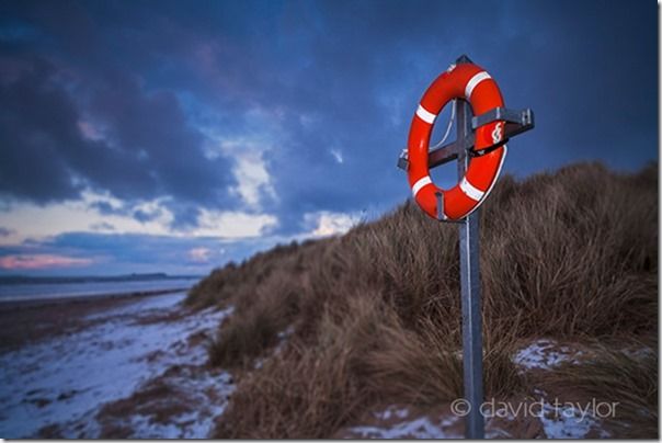 Lifebelt at the edge of a sand dune on the Northumbrian coast lit by flashlight on a stormy winter evening