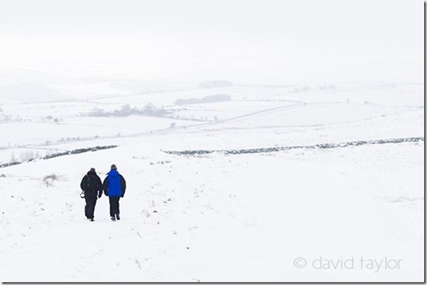 Walkers hiking across a snow-covered field near Housesteads Roman Fort in the Northumberland National Park, England